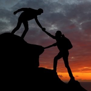 joven ayudando a otro a alcanzar la cima